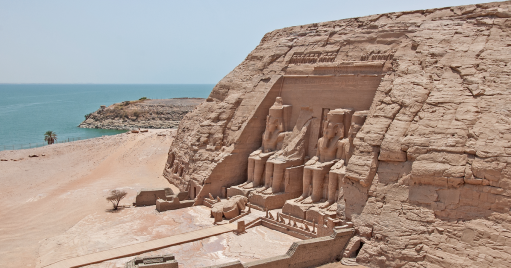 Abu Simbel Temples under a clear blue sky, with the colossal statues of Pharaoh Ramses II carved into the sandstone cliffs.