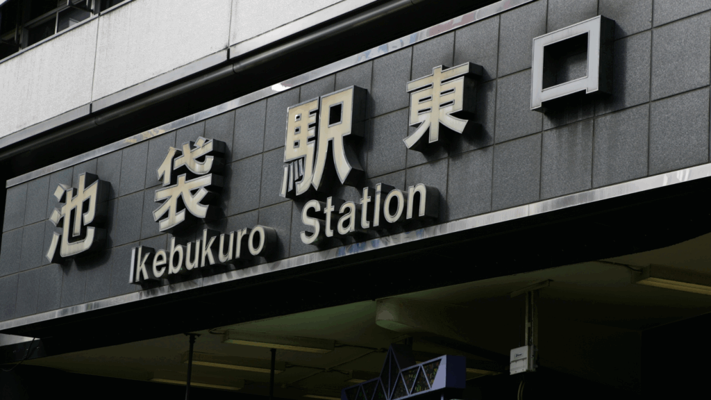 Bilingual station sign displaying both Japanese and English names at a train station in Japan.
